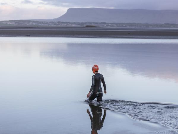 Swimmer walks in to the sea with the mountains in the background