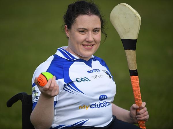 Female seated in a wheelchair holding a hurley in her left hand and a ball in her right hand