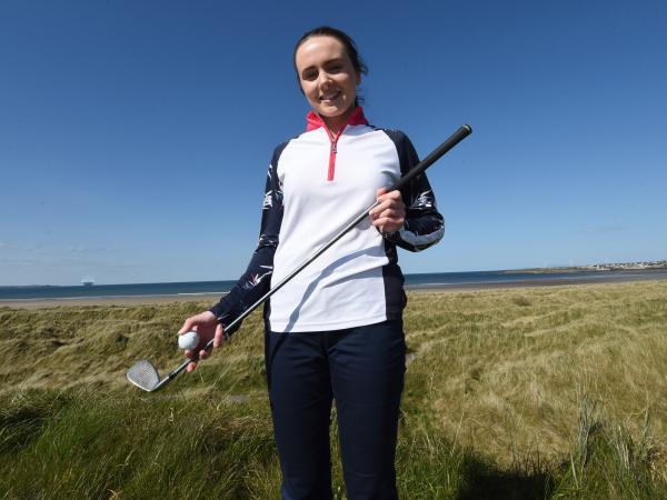 Sophie stands on a golf course holding a putter and ball