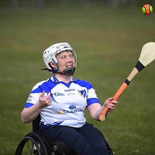 Female seated in a wheelchair hitting a ball with a hurley