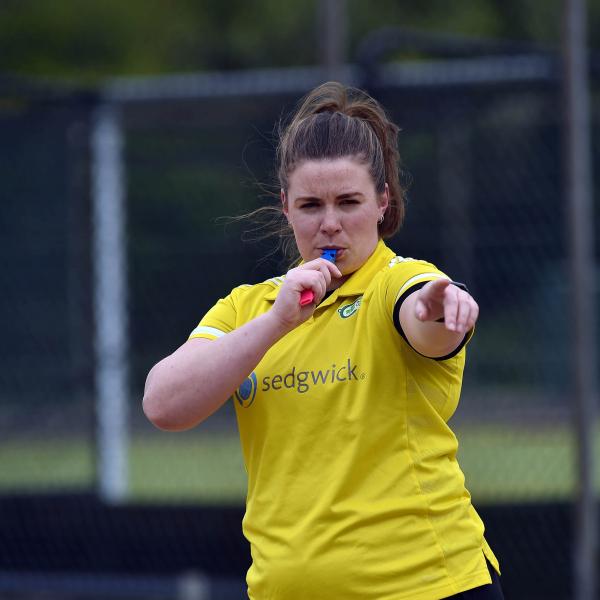 Ellie stand on the pitch, blowing the referee whistle and pointing to the left